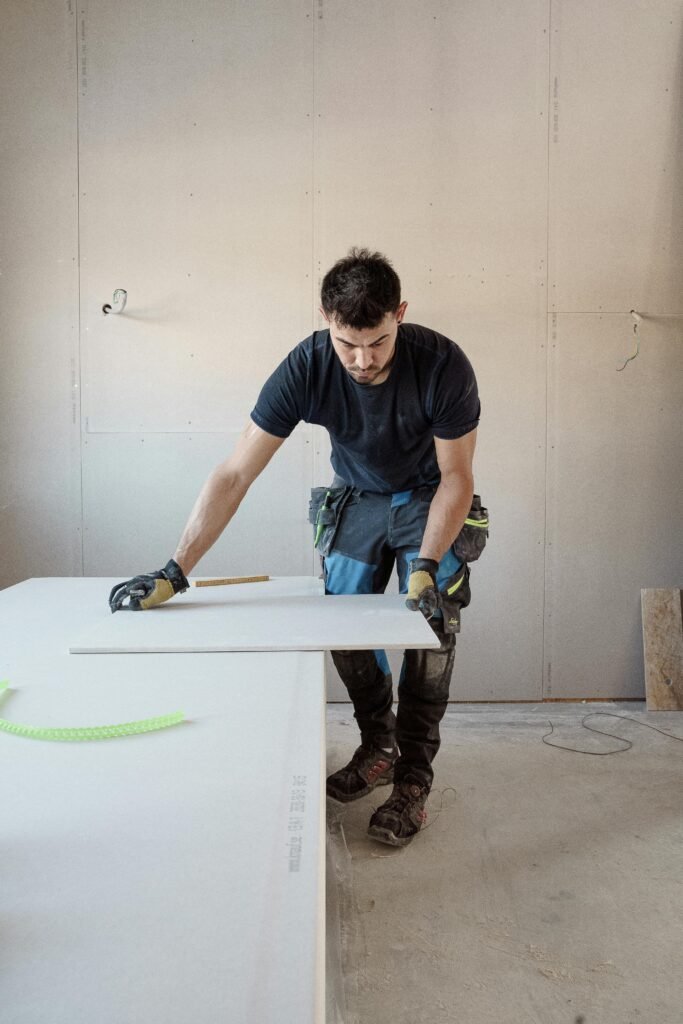 A blue collar worker measuring a plank indoors in a bright workshop.