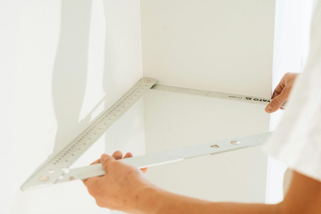 Close-up of a person measuring a corner with a metal square for home improvement or carpentry.